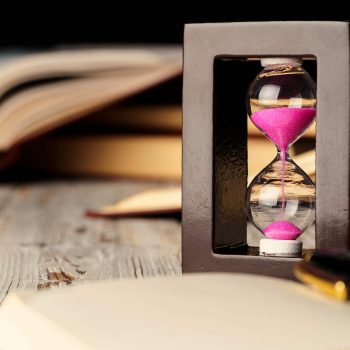 Sandglass on wooden table with opened book close up