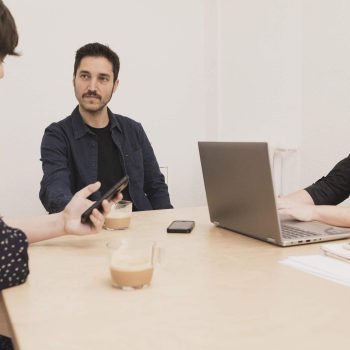 Concentrated young male near lady browsing on mobile phone and typing on laptop at table in office
